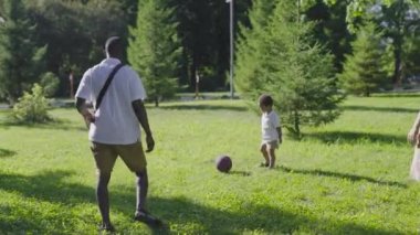 Parkta çok ırklı bir aile var. Anne sarışın ve Afrikalı Amerikalı koca oğluyla futbol oynuyor..