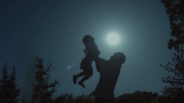 Siluetas del Padre y del Hijo al atardecer. El hombre felizmente arroja al niño y lo atrapa.. — Vídeos de Stock