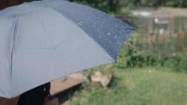 Güneşli bir günde yaz yağmuru. Gri şemsiyenin yüzeyinden su damlaları akıyor..