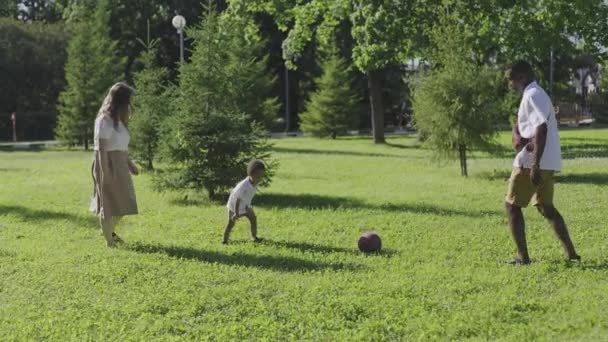 Multietnisk familj i parken. Mamma blond och afroamerikansk man spelar fotboll med sin son. — Stockvideo