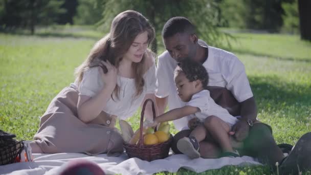 Eine niedliche multikulturelle Familie hatte ein Picknick im Park. Mutter, Vater und Sohn saßen auf einer Decke neben einem Korb mit Lebensmitteln. — Stockvideo