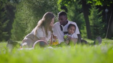 Siyah baba, açık tenli anne ve parkta mestizo çocuk. Parkta piknik yapan mutlu bir aile. Neşeli