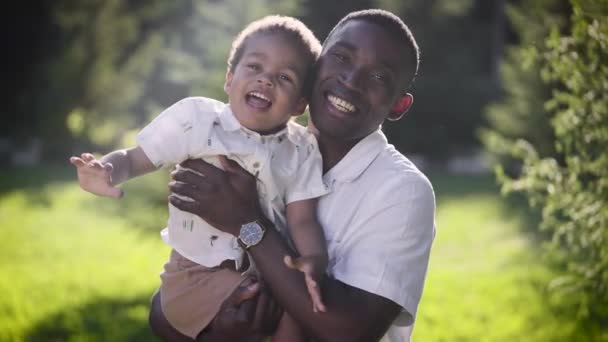 Portret van een Afrikaanse man met zijn zoon. Vader en zoon in het park in een goede bui. — Stockvideo
