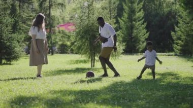 Parkta çok ırklı bir aile var. Anne sarışın ve Afrikalı Amerikalı koca oğluyla futbol oynuyor..