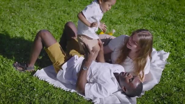 O familie multiculturală se află în parc. Tatăl negru, băiatul cu jumătate de rasă și mama se bucură de o zi de vară. . — Videoclip de stoc