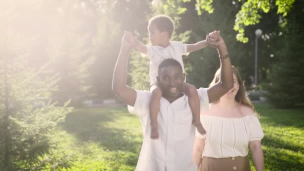 Mutlu ırklar arası aile parkta yürüyor. Anne, baba ve oğul yaz gününün tadını çıkarıyorlar.. — Stok video