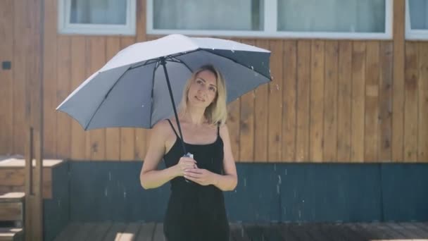 Attractive blonde in the summer rain. A pretty woman uses an umbrella to protect herself from a rainstorm. — Stock Video