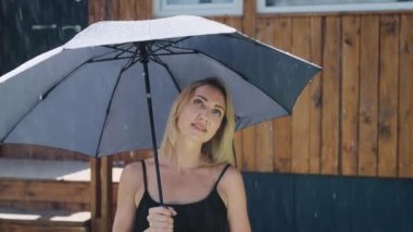 Yaz yağmurunda çekici bir sarışın. Güzel bir kadın yağmur fırtınasından korunmak için şemsiye kullanır..