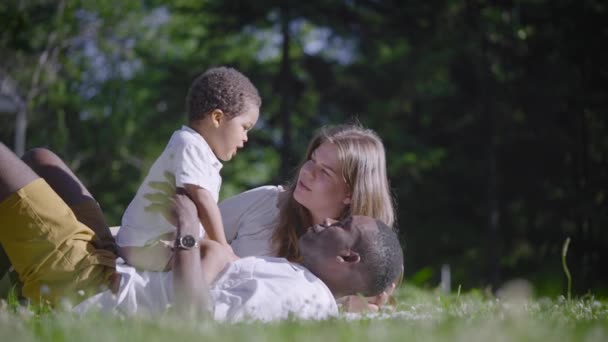 W parku znajduje się wielokulturowa rodzina. Czarny ojciec, mieszaniec i matka cieszą się letnim dniem.. — Wideo stockowe