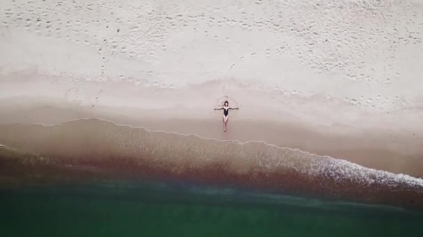 Luftaufnahme. Eine schöne Frau im schwarzen Badeanzug liegt am Strand in der Nähe des Meeres. — Stockvideo