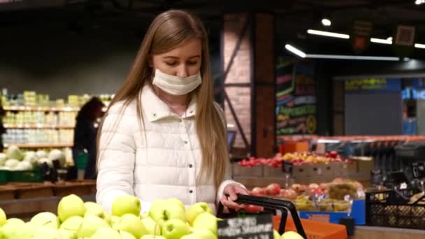 Νεαρή γυναίκα με ιατρική μάσκα αγοράζει φρούτα. Ανακοίνωση κατάστασης αυτοαπομόνωσης — Αρχείο Βίντεο