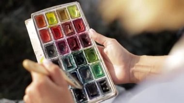 Kız elinde fırçalarla ayakta duruyor ve bir resim çiziyor..