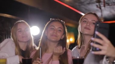 Kız arkadaşlar bir kafede oturup selfie çekerler. Gülümseyen genç kızlar