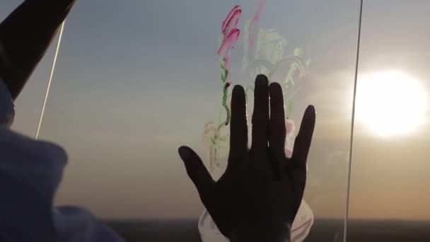 Ragazza dipinge un quadro con la mano sul vetro al tramonto — Video Stock