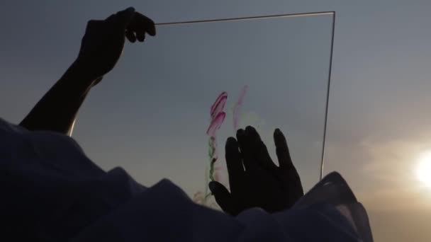 Mädchen malt ein Bild mit seiner Hand auf das Glas bei Sonnenuntergang — Stockvideo