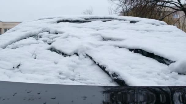 Kierowca wykopuje samochód ze śniegu w pobliżu domu. Skrobanie śniegu i lodu z przedniej szyby. Kobieta czyści samochód ze śniegu pędzlem. — Wideo stockowe