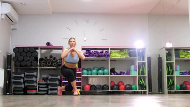 Närbild porträtt av atletisk ung kvinna gör knäböj med gummiband träning pumpa glutes. Kvinna gör fitness aerobic övningar för byte i vardagsrummet. En hälsosam livsstil. sträckning — Stockvideo