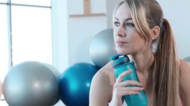 Spor giyimli genç bir kadın spor salonunda sabah antrenmanından sonra dinleniyor.