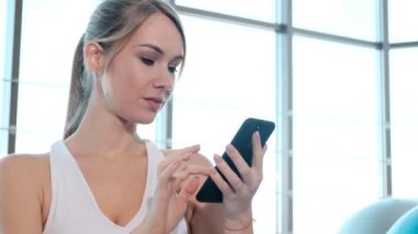 Spor salonunda akıllı telefon kullanan bir bayan atlet.
