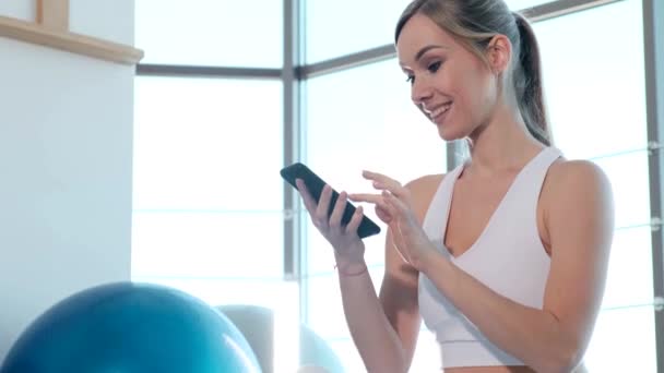 Portrait of beautiful athlete girl using smartphone in fitness center. — Stock Video