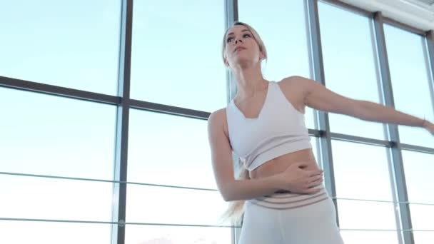 Дівчина в спортивному одязі виконує вправи в яскравій студії — стокове відео
