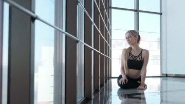 Geniş bir pencerenin yakınındaki bir odada yoga egzersizleri yapan genç bir kadın..