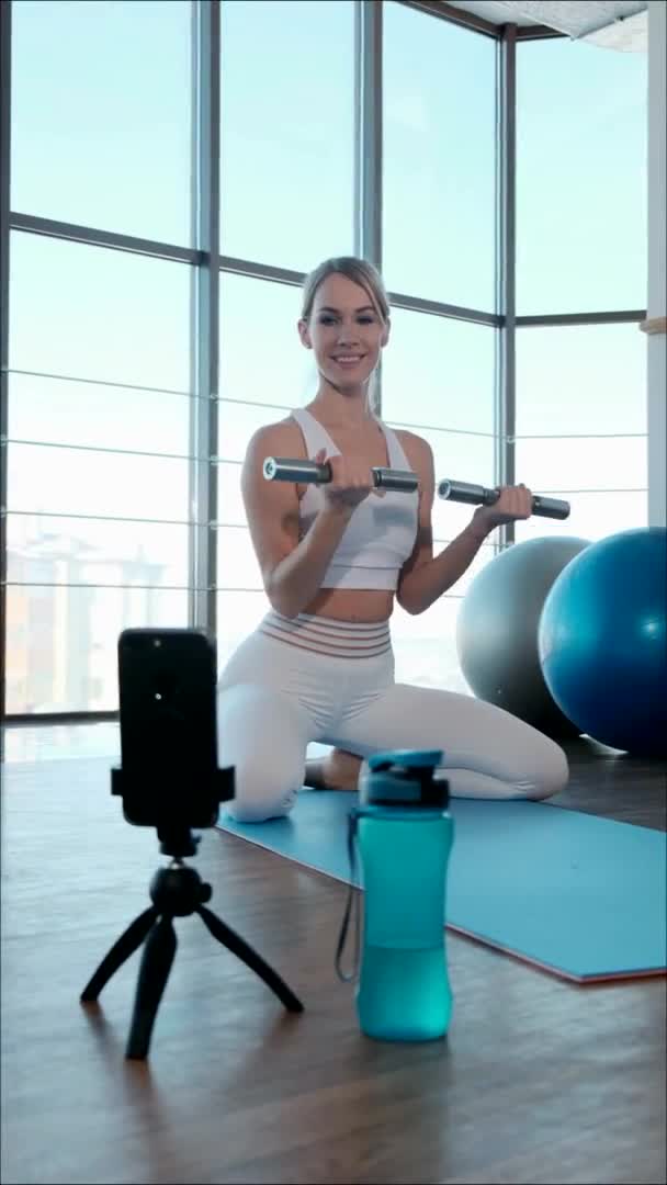 Treinador menina mostra exercícios com halteres na Internet usando um smartphone. — Vídeo de Stock