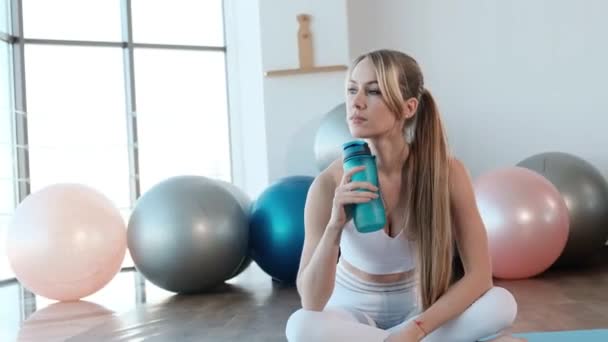 Young sports girl is resting after a hard workout in the gym and holding a bottle of water. — ストック動画