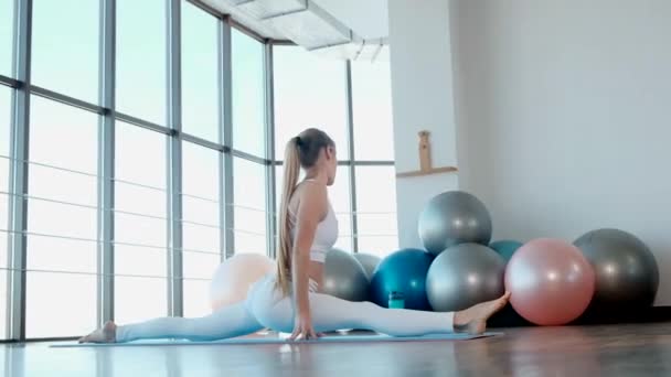 Фитнес-девушка в спортивной одежде растягивает ноги в современной студии спортзала. — стоковое видео