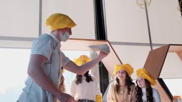 戴着黄帽的孩子们在厨房里帮忙做披萨. — 图库视频影像