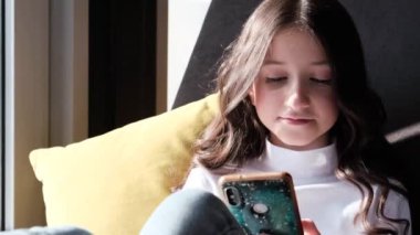 Güzel, neşeli kız pencerede oturmuş telefonla konuşuyor..