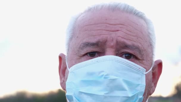 Een oudere man met een medisch masker kijkt naar de camera. — Stockvideo