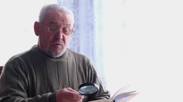 Uomo anziano che legge un libro vicino alla finestra. — Video Stock
