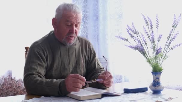 Uomo anziano che legge un libro vicino alla finestra. — Video Stock