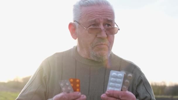 Vieil homme aux cheveux gris avec des pilules dans les mains. — Video