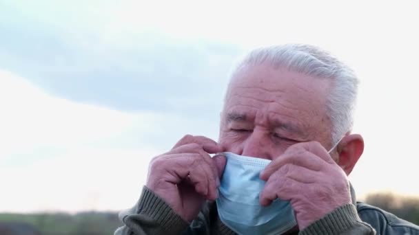 Retrato de um homem de cabelos grisalhos sênior em uma máscara médica em um contexto de luz solar. — Vídeo de Stock