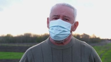 Tıbbi maskeli yaşlı bir adam kameraya bakar..