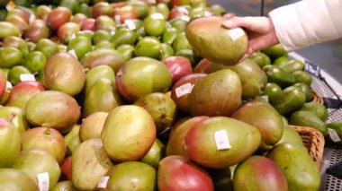 Genç kadın meyve pazarından mango alır..