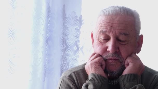 Ένας γκριζομάλλης γέρος κάθεται σκεπτικός με το πρόσωπό του καλυμμένο με τα χέρια του — Αρχείο Βίντεο