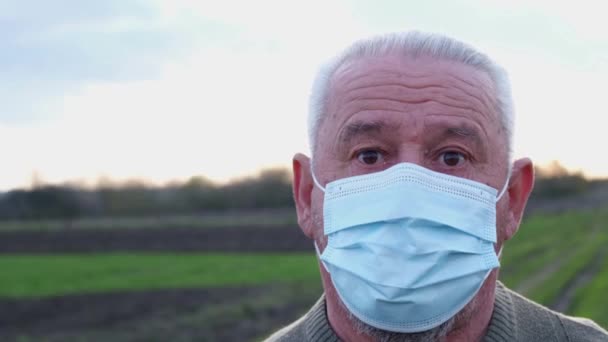 Пожилой человек в медицинской маске смотрит в камеру. — стоковое видео