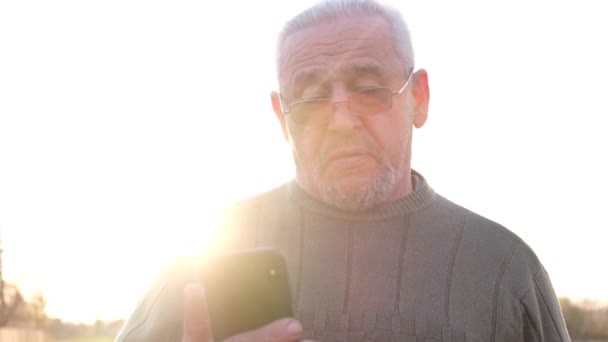Oudere man met grijs haar met een telefoon in zijn handen. — Stockvideo