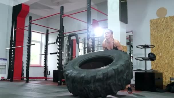 Uma mulher levanta um pneu grande em um campo de relva artificial durante o exercício - exercício de fitness crossfit — Vídeo de Stock