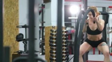 Sporcu kadın savaş halatlarıyla egzersiz yaparak spor salonunda çalışıyor..