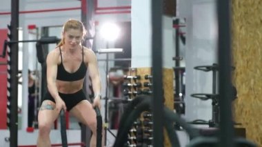 Sporcu kadın savaş halatlarıyla egzersiz yaparak spor salonunda çalışıyor..