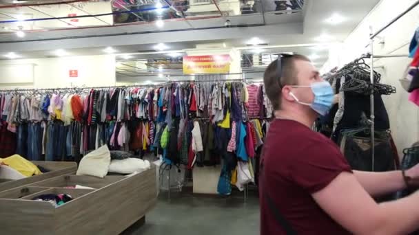 И люди выбирают одежду в магазине. Много вещей на вешалках. — стоковое видео