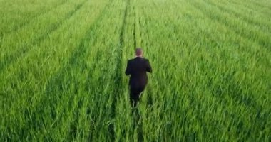 Takım elbiseli bir adam sahada koşuyor ve yüksek bir yerden ateş ediyor.