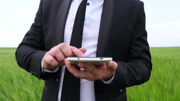 Joven hombre de negocios usando una tableta en un campo de trigo verde. — Vídeos de Stock