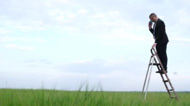 Bir adam akıllı telefonunu merdivenle kaldırarak cep telefonu sinyalini yakalamaya çalışır.