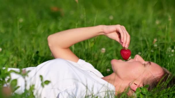 Ένα νεαρό κορίτσι δοκιμάζει φράουλες. Χαλαρώστε στη φύση στον κήπο. — Αρχείο Βίντεο