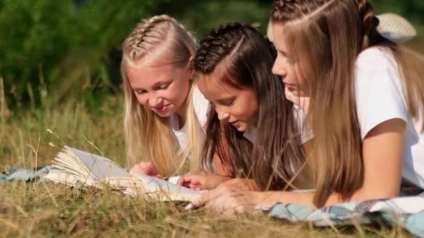 Tres chicas tumbadas en la hierba leyendo un libro en el bosque. — Vídeos de Stock